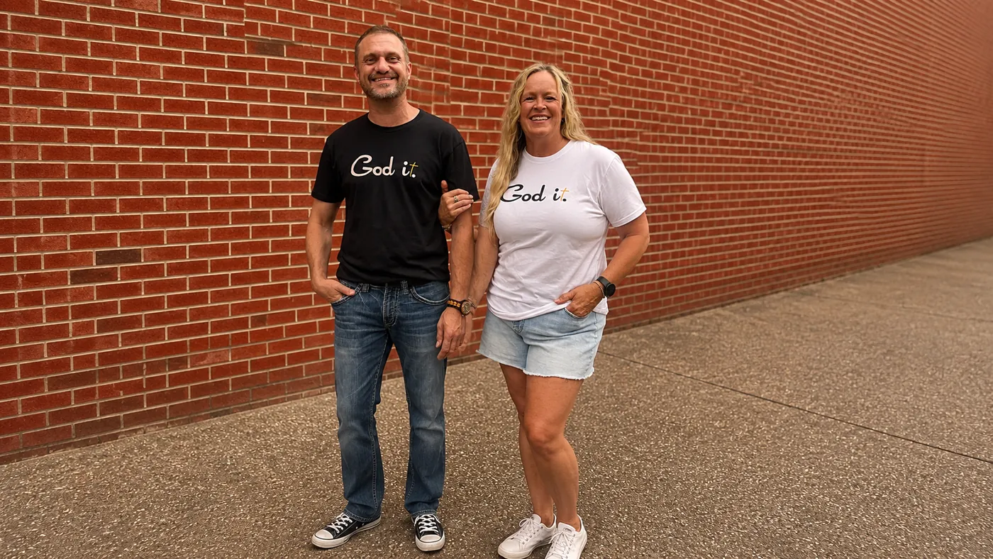Couple wearing God it. tees in front of a red brick wall